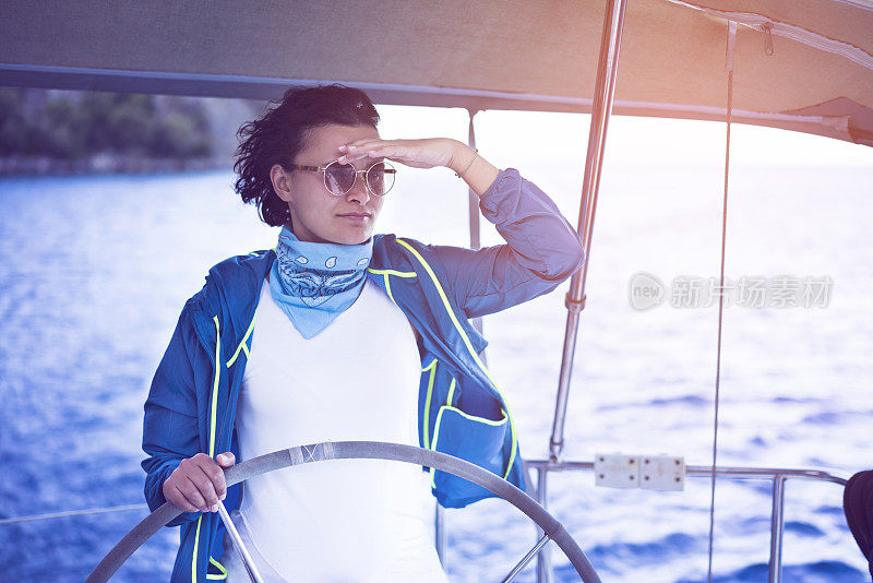 Woman standing behind the sailing wheel on a boat, sailing.